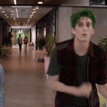 a man with green hair and a plaid vest is walking down a hallway