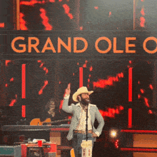 a man in a cowboy hat stands on stage in front of a sign that says grand oleo