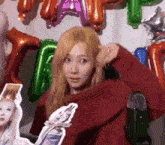 a woman in a red sweater is standing in front of balloons and a picture of herself .