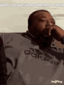 a man wearing an adidas shirt is covering his mouth with his hand
