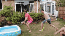 a woman in a pink shirt is jumping over a man in blue shorts