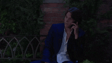 a man in a suit is talking on a cell phone while sitting in a chair .