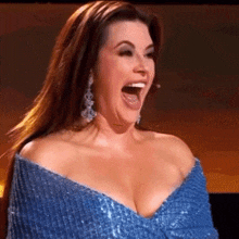 a woman in a blue dress is laughing with her mouth open and earrings .
