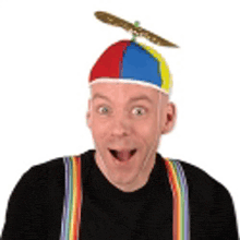a man wearing a colorful hat with a propeller on top of it and suspenders .