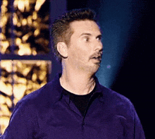a man in a purple shirt is standing in front of a microphone on a stage .