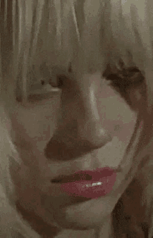 a close up of a woman 's face with blonde hair , red lips and a necklace .