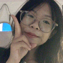 a woman wearing glasses holds her hand to her chin