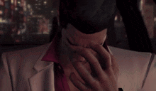 a man in a white suit covering his face with his hand