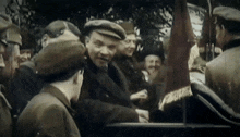 a man in a hat stands in a crowd with a flag that says ' lenin ' on it