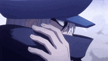 a person covering their face with their hand while wearing a blue hat