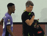 a man holding a bottle of water stands next to a man in a purple shirt that says scher
