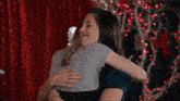 two women are hugging each other in front of a red curtain with christmas lights .