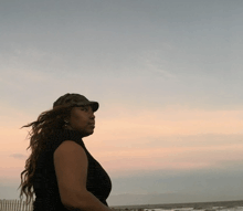 a woman wearing a hat stands on the beach