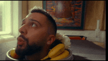 a man with a beard is sitting at a table with a bowl of fruit on his head