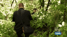 two men are walking through the woods with a travel channel logo in the background