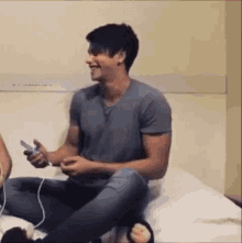 a man is sitting on a bed playing a video game with a controller .