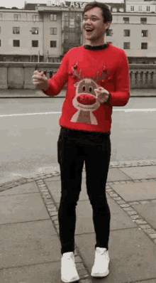 a man wearing a red reindeer sweater is standing on a sidewalk .