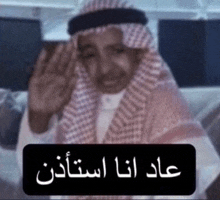 a man in a keffiyeh is waving his hand in front of a sign with arabic writing on it