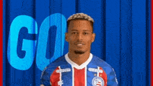 a man in a soccer uniform is standing in front of a blue wall with the word go behind him .