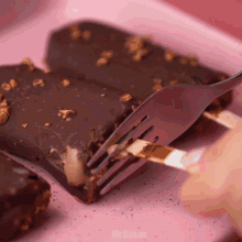 a person is holding a fork over a chocolate bar on a pink plate