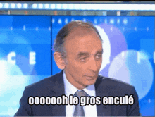 a man in a suit and tie is sitting in front of a blue screen that says 000000h le gros encule