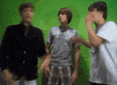three young men are standing next to each other in front of a green background .