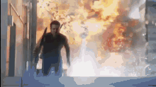 a man in a black shirt is standing in front of a large explosion .