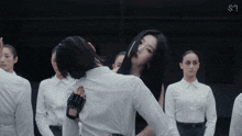 a group of women in white shirts are standing in a dark room with the letter s on the bottom right