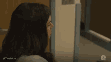 a woman is standing in a hallway next to a door and looking out the window .
