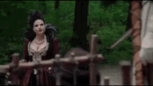a woman in a red dress is standing next to a wooden wagon in the woods .