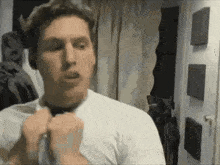 a man in a white shirt is adjusting his tie while standing in a room .