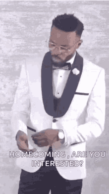 a man in a white tuxedo and bow tie is looking at his watch .