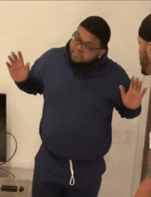 a man in a blue hoodie is standing in front of a television with his hands outstretched
