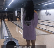a woman in a purple shirt stands in a bowling alley with the number 8 on the wall behind her