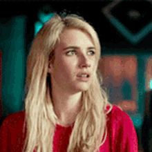 a woman with blonde hair is wearing a red sweater and looking at the camera .