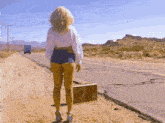 a woman in shorts is walking down a dirt road with a suitcase