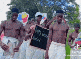 a group of shirtless men are standing in a field holding a sign that says happy birthday alacard .