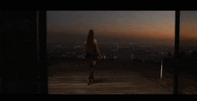 a woman is standing on a balcony overlooking a city at night