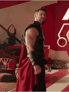 thor is standing in a room wearing a red cape and armor .