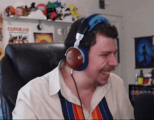 a man wearing headphones is smiling in front of a poster that says cuphead