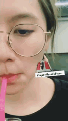 a woman wearing glasses is drinking through a pink straw with a sticker that says ' en ' on it