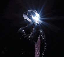 a man wearing a black sequined jacket and a white hat holds a light in his hand