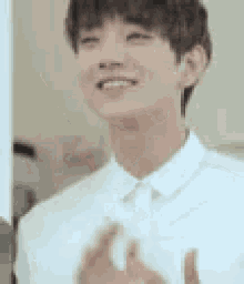 a young man in a white shirt is smiling and clapping his hands in front of a mirror .