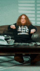 a man sitting on a couch wearing a black shirt that says ' a few dollars ' on it