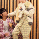 a man in a plaid shirt is standing next to another man holding a stuffed animal