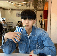 a young man in a denim jacket is drinking from a cup with a straw ..