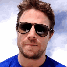 a man wearing a blue shirt and ray-ban sunglasses looks at the camera