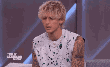 a man wearing a pearl necklace is sitting on a couch on the kelly clarkson show