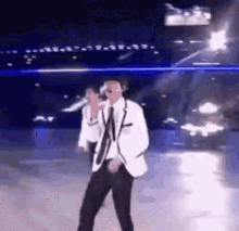 a man in a suit and tie is dancing on a stage while holding a microphone .