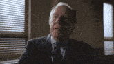 an older man in a suit and tie is sitting in front of a window